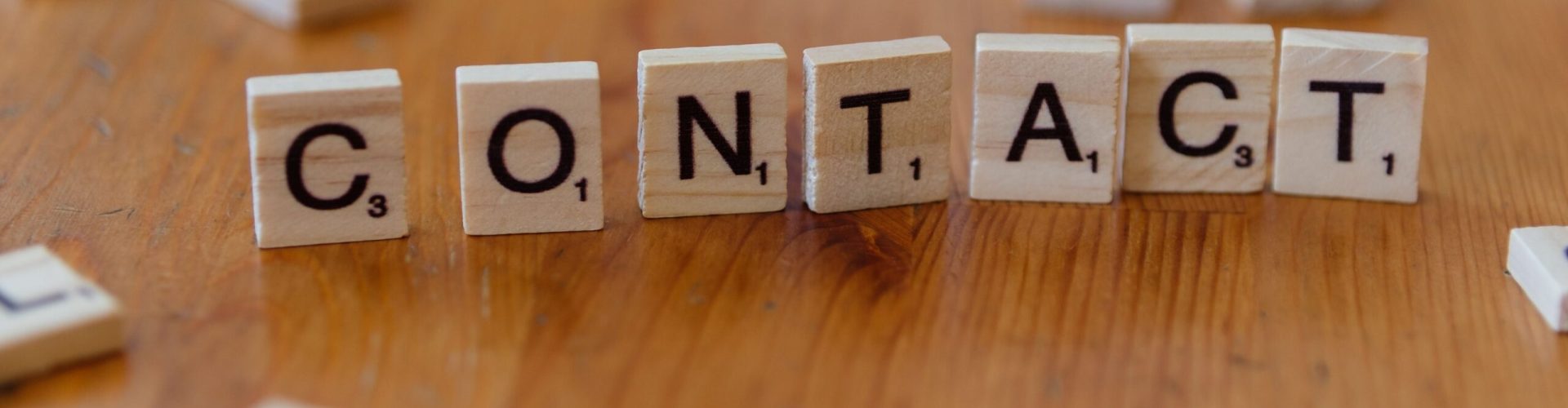 Scrabble letters spelling 'contact' on a wooden table surface.